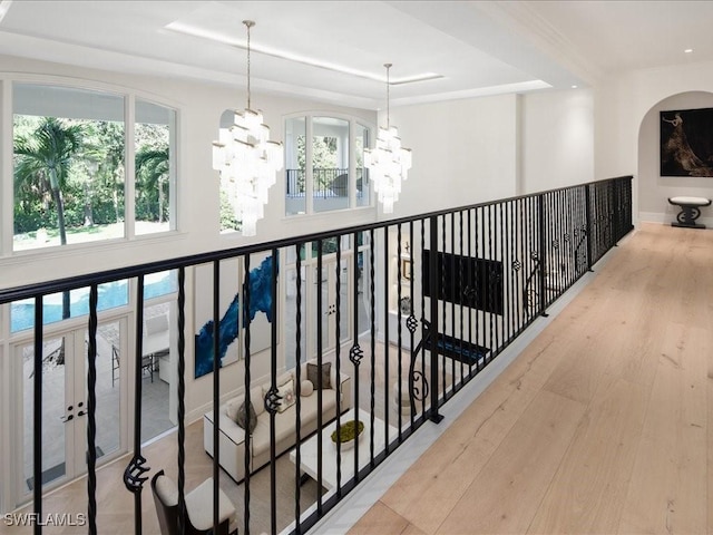 corridor featuring a notable chandelier, a tray ceiling, baseboards, and wood finished floors