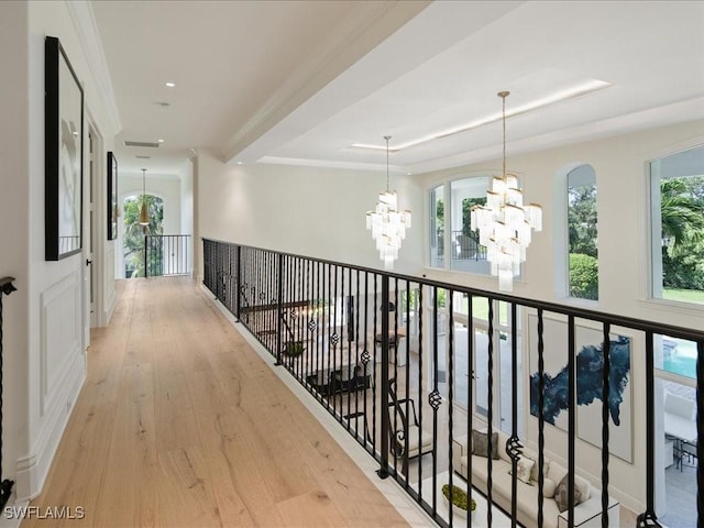 hall featuring light wood-style flooring, a tray ceiling, a chandelier, and a wealth of natural light