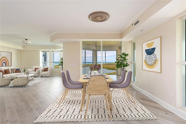 dining space featuring ornamental molding, a water view, and light wood-type flooring