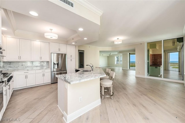 kitchen featuring a breakfast bar, a kitchen island with sink, light stone countertops, white cabinets, and stainless steel fridge