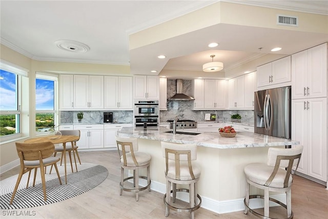 kitchen with tasteful backsplash, wall chimney range hood, white cabinetry, light stone countertops, and appliances with stainless steel finishes