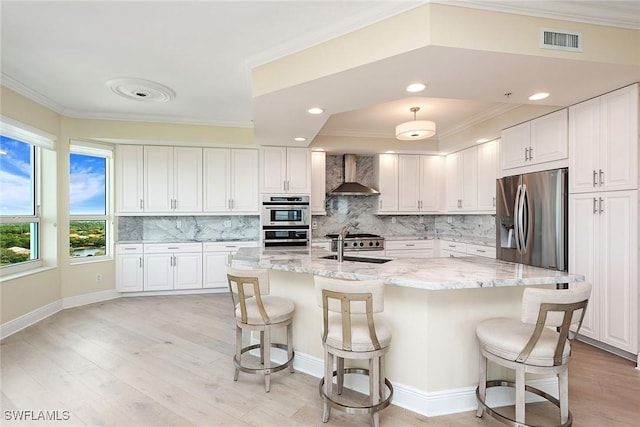 kitchen with stainless steel appliances, wall chimney exhaust hood, white cabinetry, and light stone counters