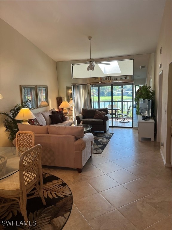 living room with lofted ceiling with skylight, light tile patterned flooring, and ceiling fan