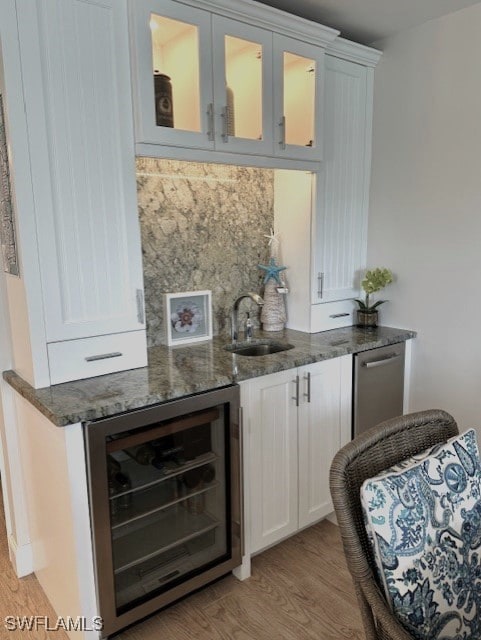 bar with white cabinets, beverage cooler, light wood-type flooring, dark stone countertops, and sink