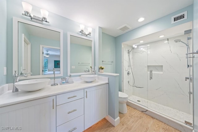 bathroom with toilet, wood-type flooring, walk in shower, vanity, and ceiling fan