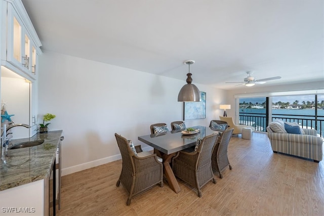 dining area with sink, a water view, light wood-type flooring, and ceiling fan