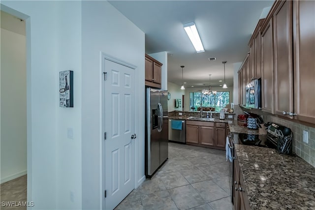 kitchen featuring kitchen peninsula, appliances with stainless steel finishes, dark stone countertops, sink, and decorative light fixtures