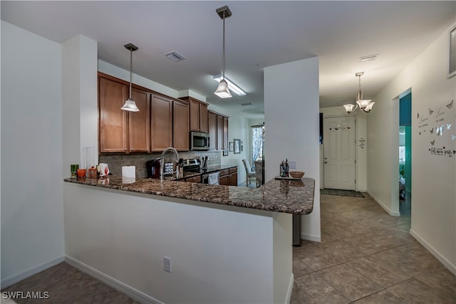 kitchen with decorative backsplash, hanging light fixtures, kitchen peninsula, dark stone countertops, and appliances with stainless steel finishes