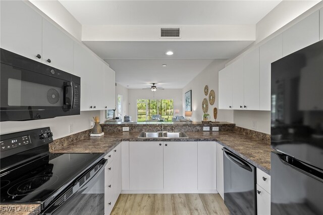 kitchen featuring light hardwood / wood-style floors, dark stone countertops, white cabinets, black appliances, and sink