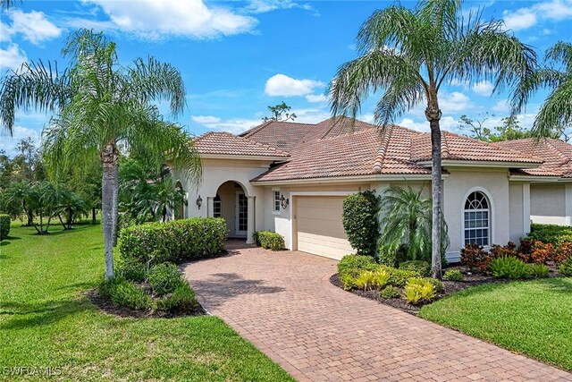 mediterranean / spanish home featuring a garage, a tiled roof, decorative driveway, stucco siding, and a front yard