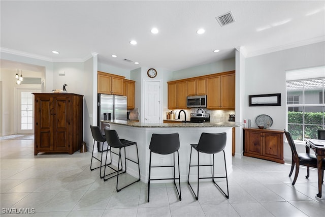 kitchen featuring visible vents, an island with sink, a breakfast bar area, stainless steel appliances, and backsplash