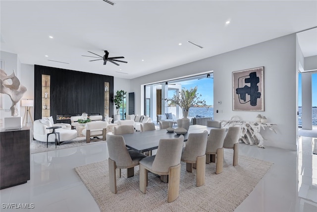 dining room with ceiling fan, a large fireplace, a water view, and light tile patterned floors