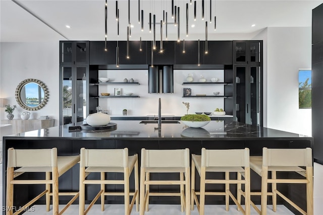 kitchen with a large island with sink, dark stone counters, a kitchen breakfast bar, and sink