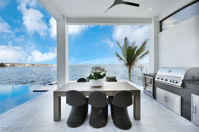 view of patio featuring an outdoor kitchen, ceiling fan, a water view, and grilling area