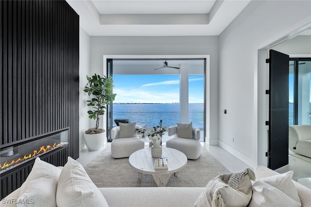 living room featuring ceiling fan, a water view, and a tray ceiling