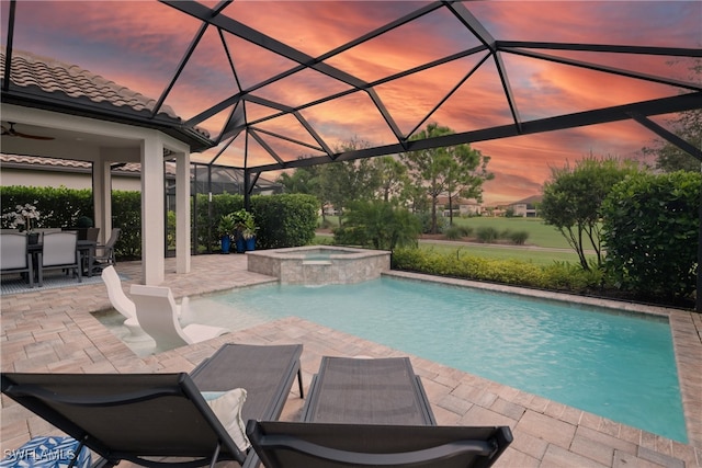 pool at dusk with ceiling fan, an in ground hot tub, a lanai, and a patio area