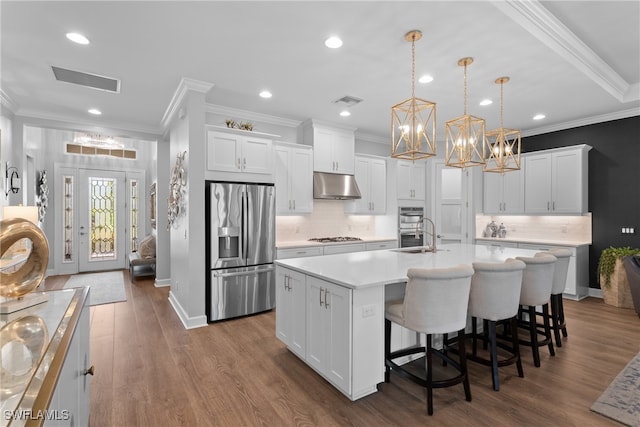 kitchen with an island with sink, appliances with stainless steel finishes, hanging light fixtures, and white cabinetry