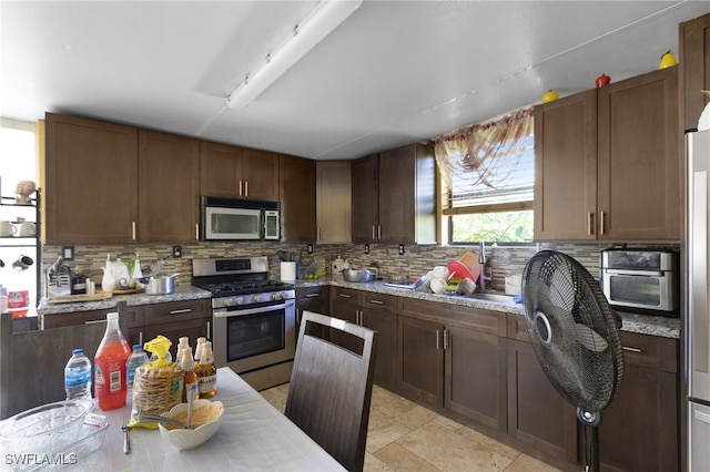 kitchen featuring appliances with stainless steel finishes, decorative backsplash, dark brown cabinetry, and light stone counters