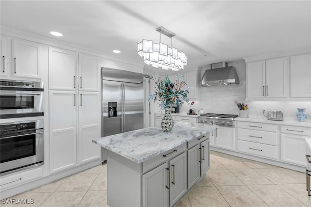 kitchen featuring a kitchen island, appliances with stainless steel finishes, white cabinetry, wall chimney exhaust hood, and decorative light fixtures