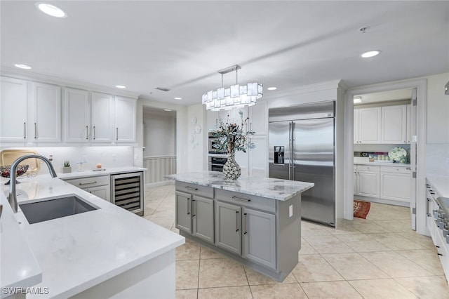 kitchen featuring a kitchen island, hanging light fixtures, built in refrigerator, sink, and beverage cooler