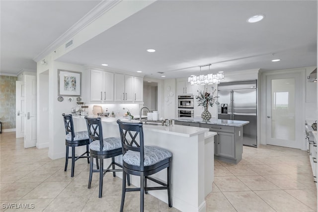 kitchen featuring a kitchen bar, stainless steel appliances, decorative light fixtures, crown molding, and a center island with sink