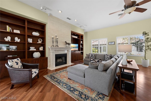 living room with a large fireplace, ceiling fan, and dark wood-type flooring