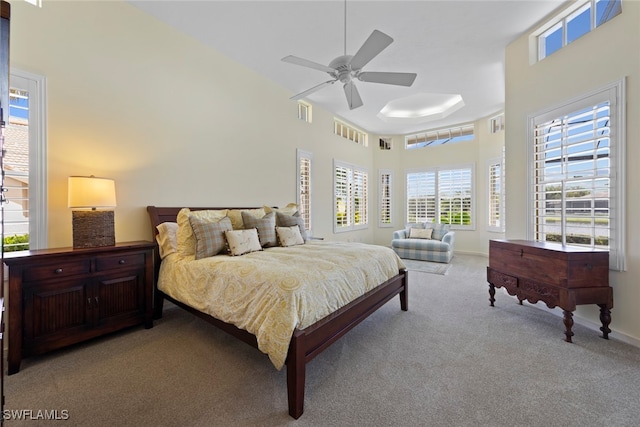 carpeted bedroom with ceiling fan, a towering ceiling, and multiple windows