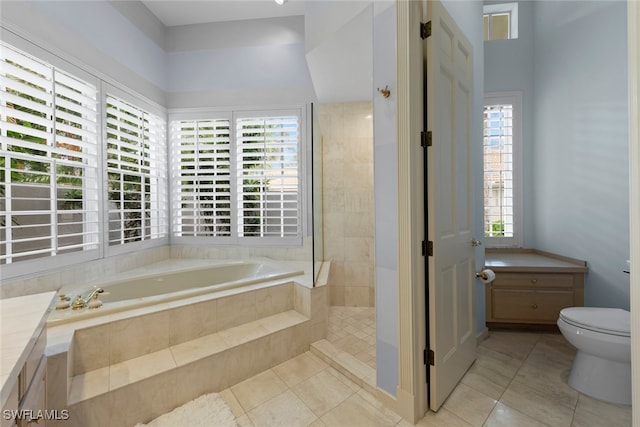 bathroom featuring a wealth of natural light, tiled tub, vanity, and toilet