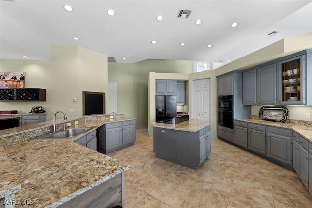 kitchen with gray cabinetry, light stone counters, black appliances, a center island, and sink