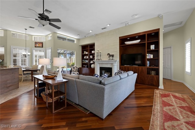 living room with built in features, ceiling fan with notable chandelier, dark wood-type flooring, and a premium fireplace