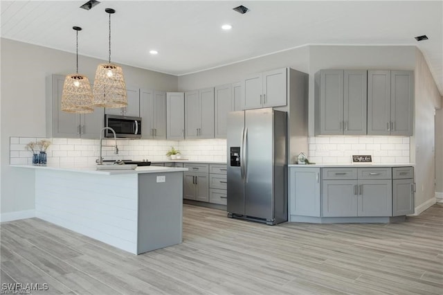 kitchen with appliances with stainless steel finishes, backsplash, kitchen peninsula, and light wood-type flooring