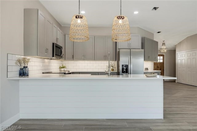 kitchen with gray cabinets, appliances with stainless steel finishes, hardwood / wood-style floors, and kitchen peninsula