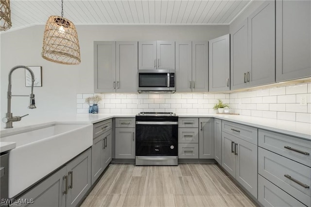 kitchen featuring gray cabinetry, backsplash, appliances with stainless steel finishes, and decorative light fixtures