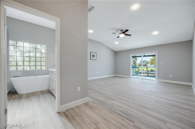 empty room with light hardwood / wood-style flooring, tile walls, vaulted ceiling, and ceiling fan