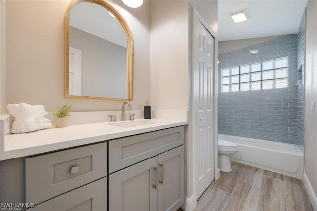 full bathroom with tiled shower / bath, vanity, toilet, hardwood / wood-style floors, and vaulted ceiling