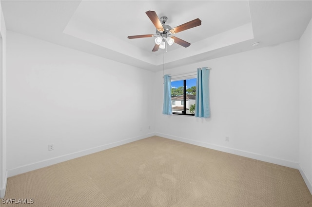 carpeted empty room featuring ceiling fan and a raised ceiling