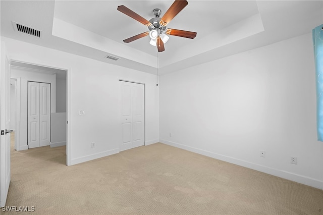 unfurnished bedroom with ceiling fan, light colored carpet, a tray ceiling, and a closet