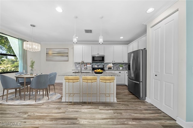 kitchen with white cabinets, pendant lighting, wood-type flooring, a center island with sink, and appliances with stainless steel finishes