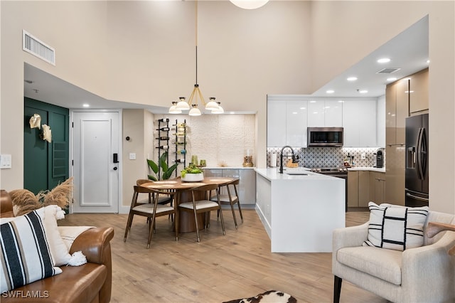 interior space with hanging light fixtures, white cabinets, light wood-type flooring, black refrigerator with ice dispenser, and sink