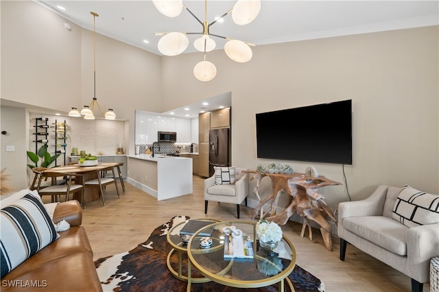 living room with an inviting chandelier, a towering ceiling, light hardwood / wood-style floors, and sink