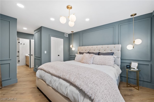 bedroom featuring connected bathroom, an inviting chandelier, and light hardwood / wood-style flooring