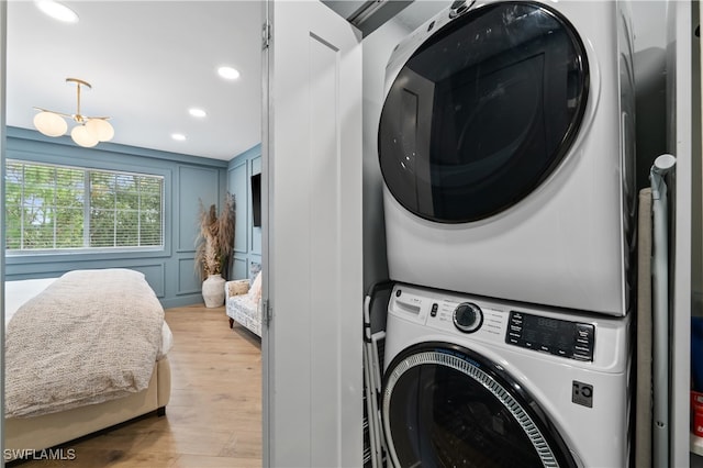 clothes washing area with an inviting chandelier, stacked washer / dryer, and light hardwood / wood-style floors