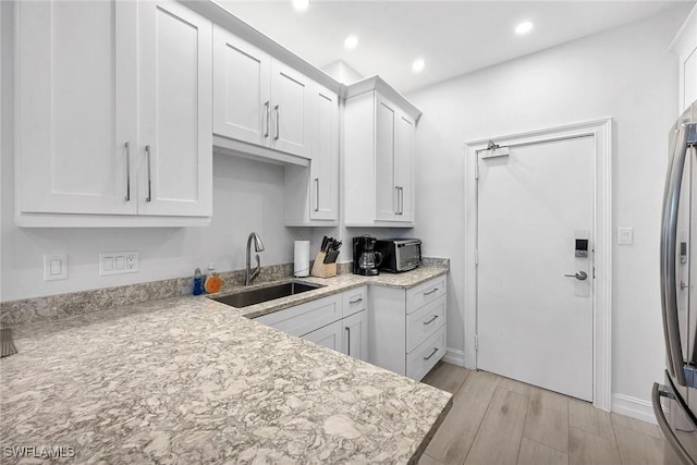 kitchen with stainless steel fridge, light stone counters, white cabinetry, and sink