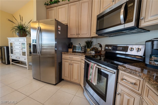 kitchen featuring light brown cabinetry, stainless steel appliances, light tile patterned floors, and dark stone counters