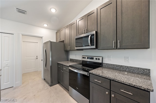 kitchen with dark stone countertops, stainless steel appliances, dark brown cabinetry, and lofted ceiling