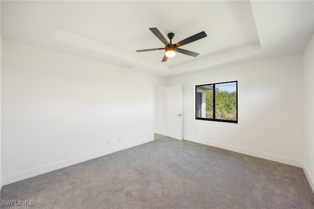 spare room with ceiling fan, a raised ceiling, and carpet flooring