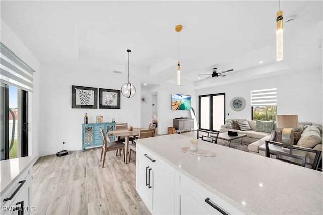 kitchen with light stone countertops, pendant lighting, light wood-type flooring, white cabinetry, and ceiling fan