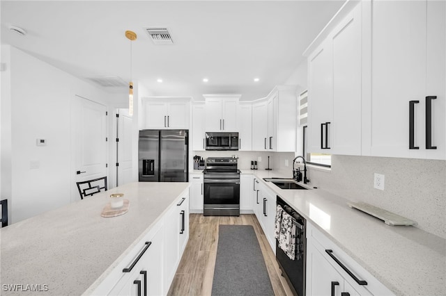 kitchen featuring appliances with stainless steel finishes, white cabinetry, light stone countertops, sink, and decorative light fixtures