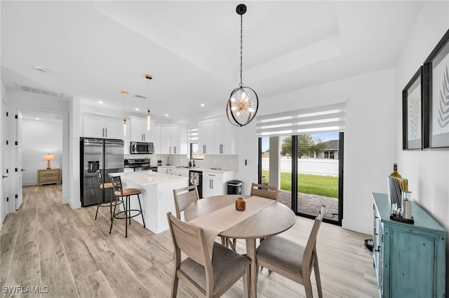 dining space featuring sink, light hardwood / wood-style flooring, and a tray ceiling