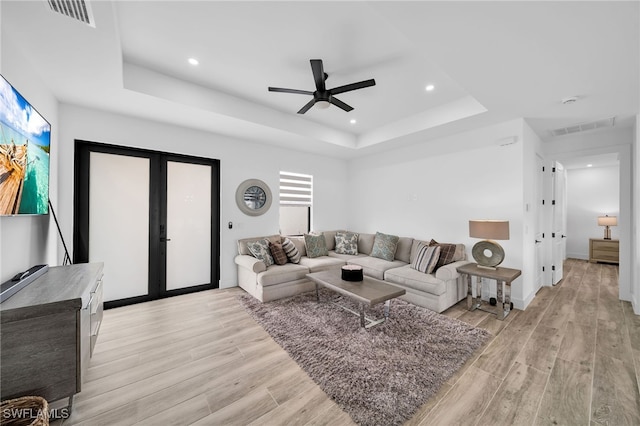 living room featuring light hardwood / wood-style floors, french doors, a raised ceiling, and ceiling fan